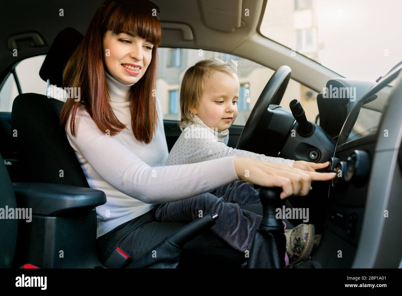Junge Mutter mit niedlichen kleinen Mädchen Kind im Auto spielen, Musik  oder Radio hören, sitzen zusammen auf dem Vordersitz in der Nähe Auto  Lenkrad Stockfotografie - Alamy