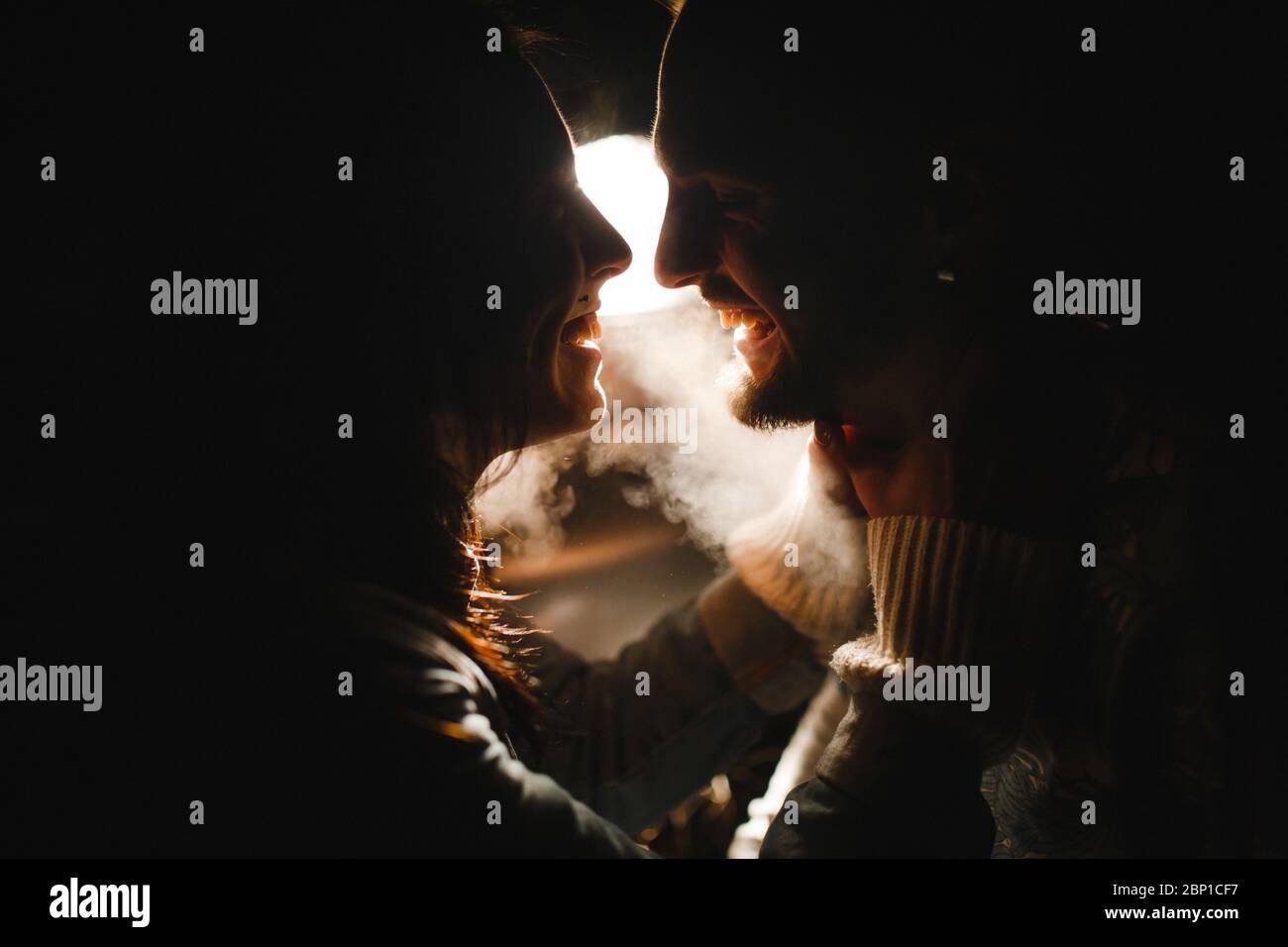 Dunkle Silhouetten des Mannes und der Frau, die vor dem Hintergrund des Lichts und des Rauchs lachen Stockfoto