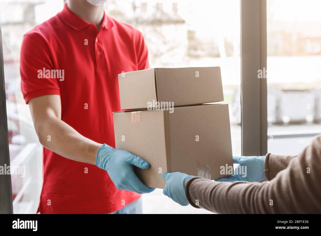 Kurier liefert Pakete in medizinischen Handschuhen zu Hause Stockfoto