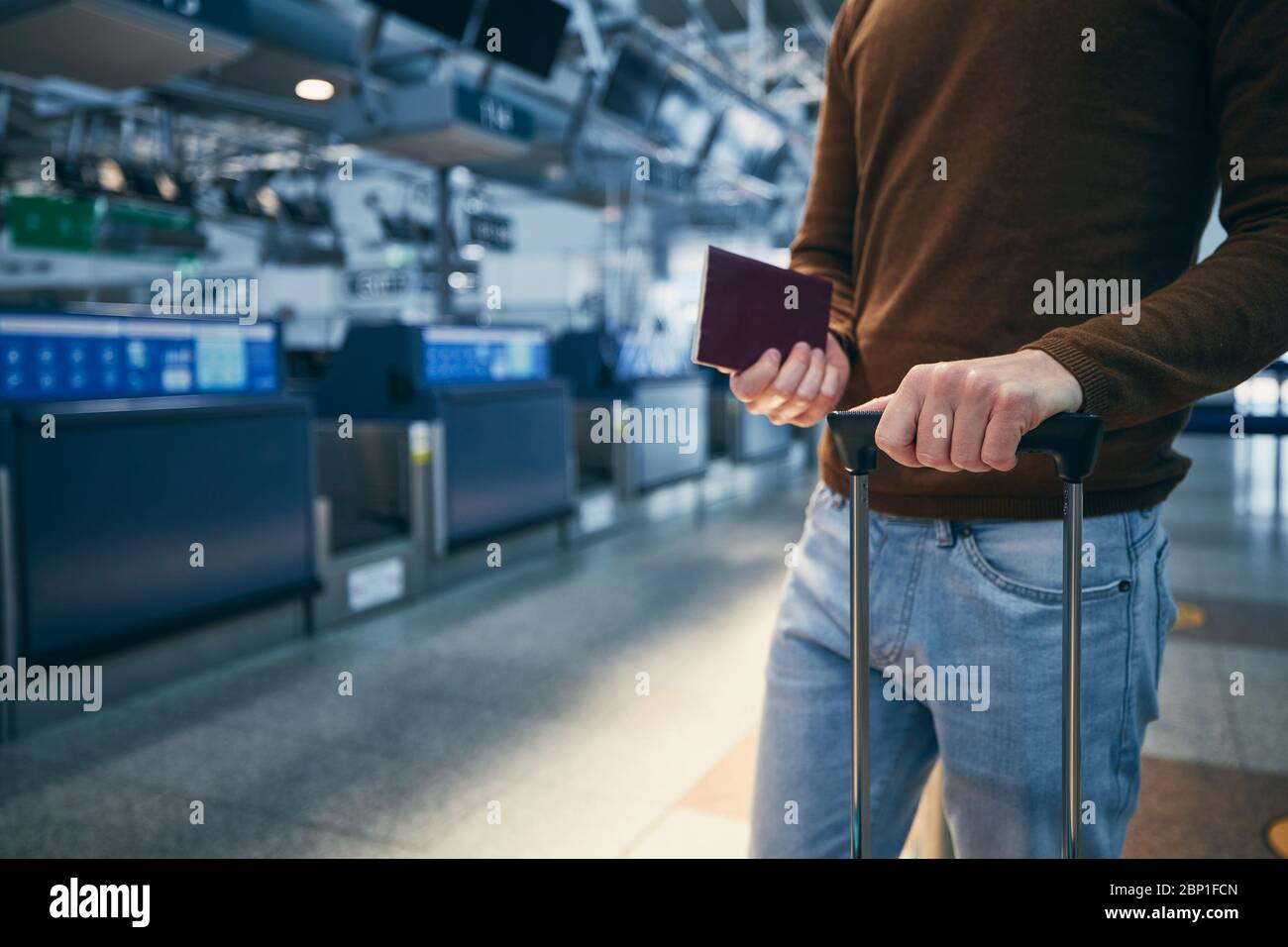 Passagier gegen Abfertigung am Flughafen. Hände eines jungen Mannes, der Koffer und Reisepass hält. Stockfoto