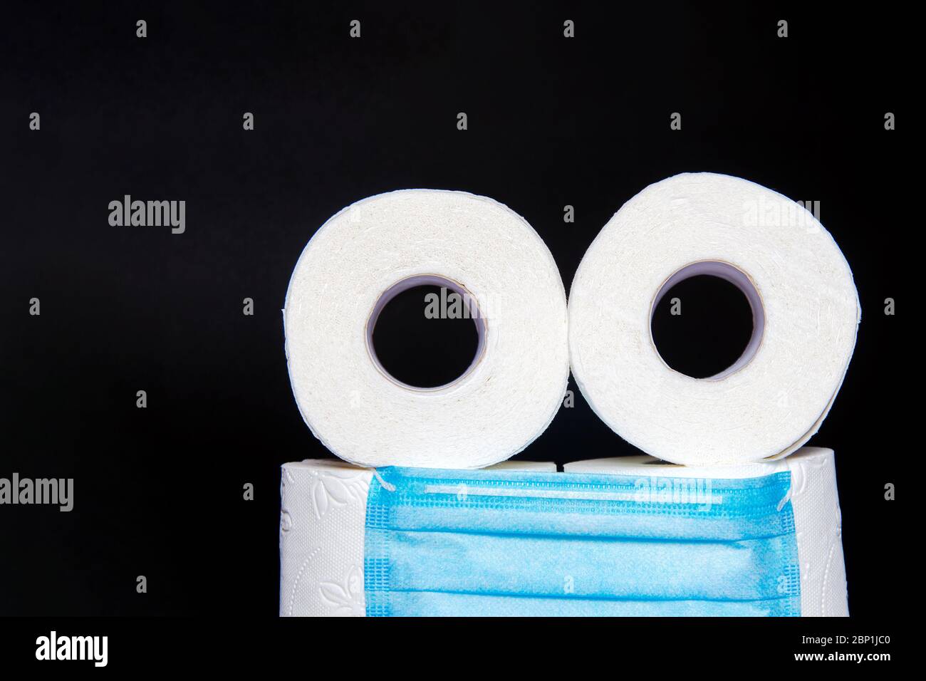 toilettenpapier Rollen mit einer medizinischen Maske in Form eines Emoticons gefaltet, auf schwarzem Hintergrund. Konzept der Panik während Coronavirus. Kopierraum Stockfoto