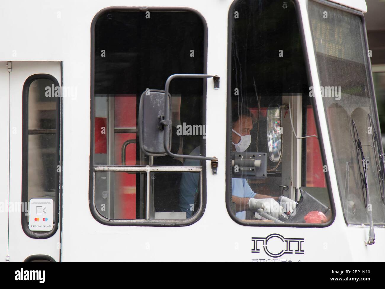 Belgrad, Serbien - 15. Mai 2020: Straßenbahnfahrer, die von außen in einer weißen Straßenbahn operativ Gesichtsmasken und Handschuhe tragen Stockfoto