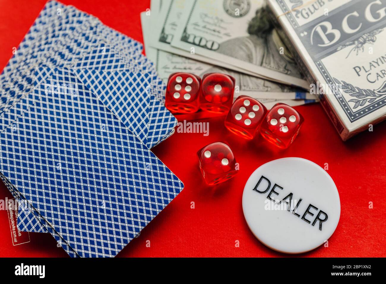 Poker-Karten, rote Würfel und Stapel von Dollar mit weißen Dealer Zeichen auf rotem Hintergrund Stockfoto