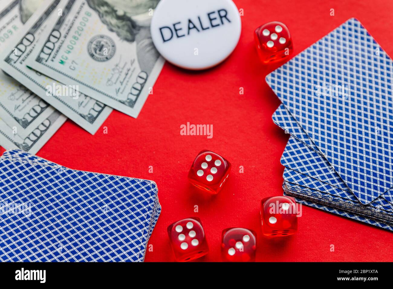 Poker-Karten, rote Würfel und Stapel von Dollar mit weißen Dealer Zeichen auf rotem Hintergrund Stockfoto