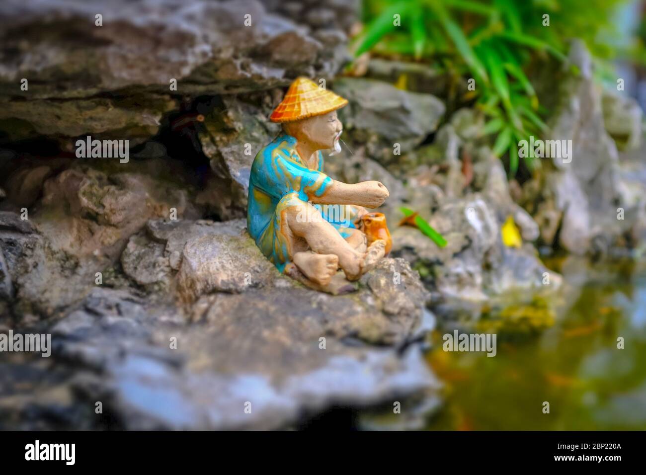 Kleine Figur, die einen Fischer in natürlicher Umgebung mit verschwommenem Grün und felsigen Hintergrund, Hanoi, Vietnam Stockfoto