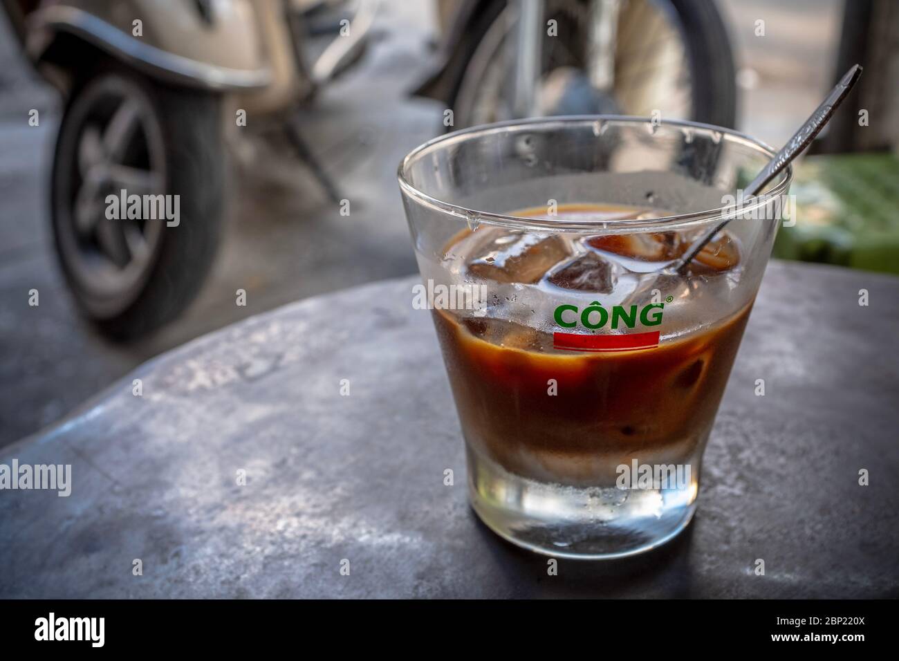 Vietnamesischer Kaffee im Glas mit Eis, mit verschwommenen Motorradrädern im Hintergrund, Hanoi, Vietnam Stockfoto