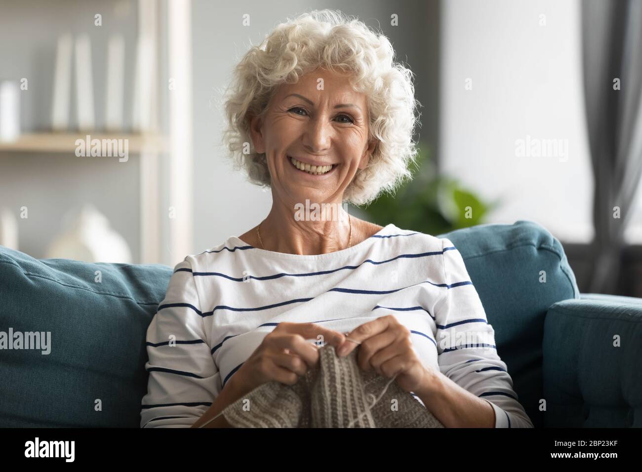 Lächelnde Frau mittleren Alters Stricken warmen Pullover mit Wollfäden. Stockfoto