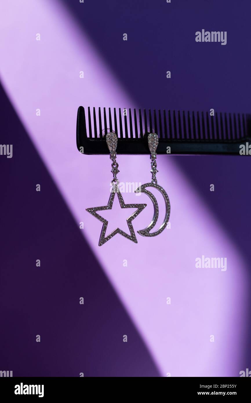 Asymmetrische Ohrringe auf einem lila Hintergrund Stockfoto