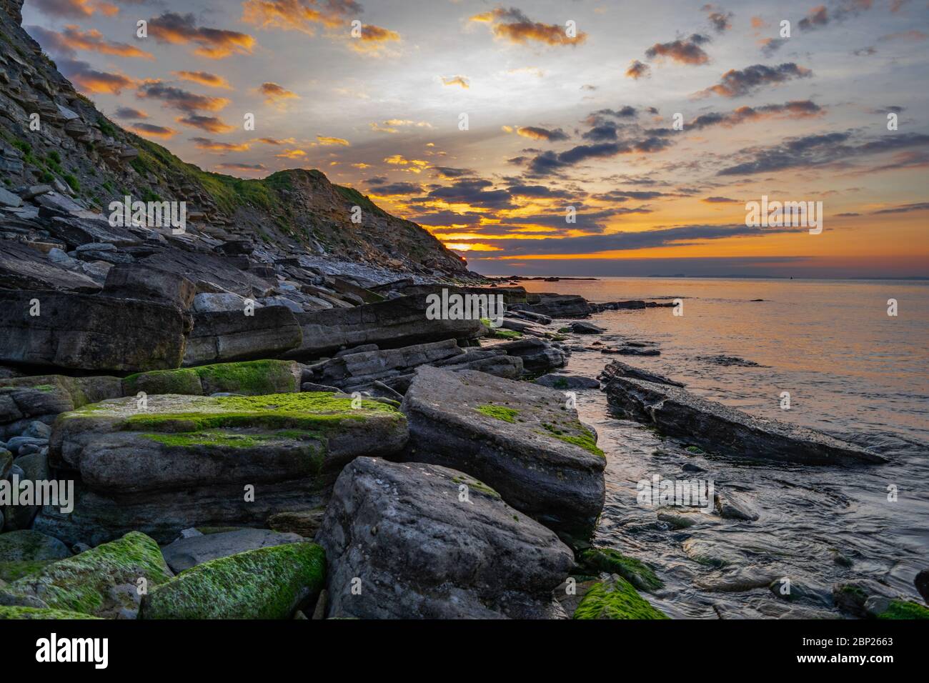 Swanage Coast (Durlston Bay) bei Sonnenaufgang mit jurassic Felsen bedeckt mit Algen und einem reichen orange Leuchten, wie die Sonne aufgeht. Swanage, Dorset, England Stockfoto