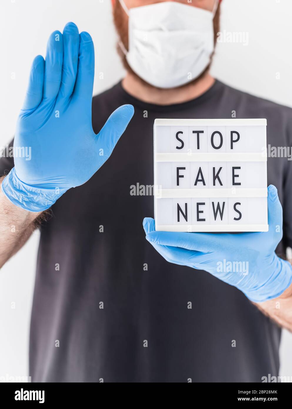 Fake News Infosemics during Covid-19 Pandemie Concept. Mann trägt Schutzmaske und medizinische Handschuhe an den Händen halten Leuchtkasten mit Text Stop Fake ne ne Stockfoto