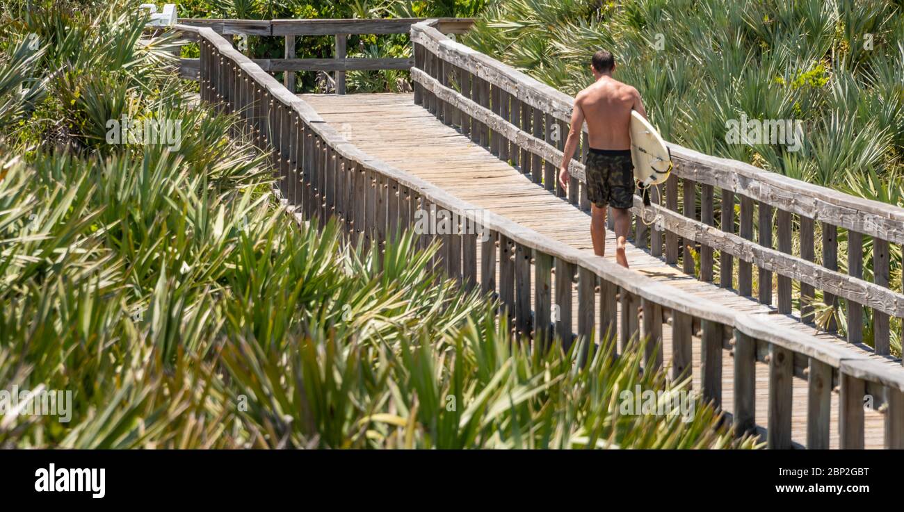 Surfer, die vom Strand über die Holzboardpromenade des Light House Point Park in Ponce Inlet, FL, zwischen Daytona Beach und New Smyrna Beach zurückkehren. (USA) Stockfoto