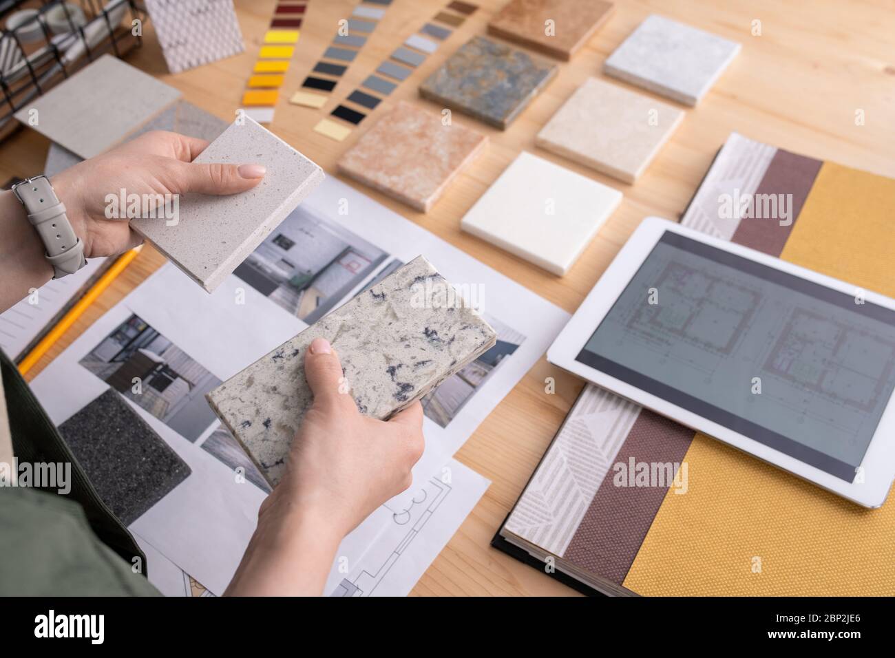 Hände der jungen Designerin hält zwei Proben von Marmorfliesen über Holztisch mit digitalen Tablet, Fotos von zu Hause Interieur etc Stockfoto