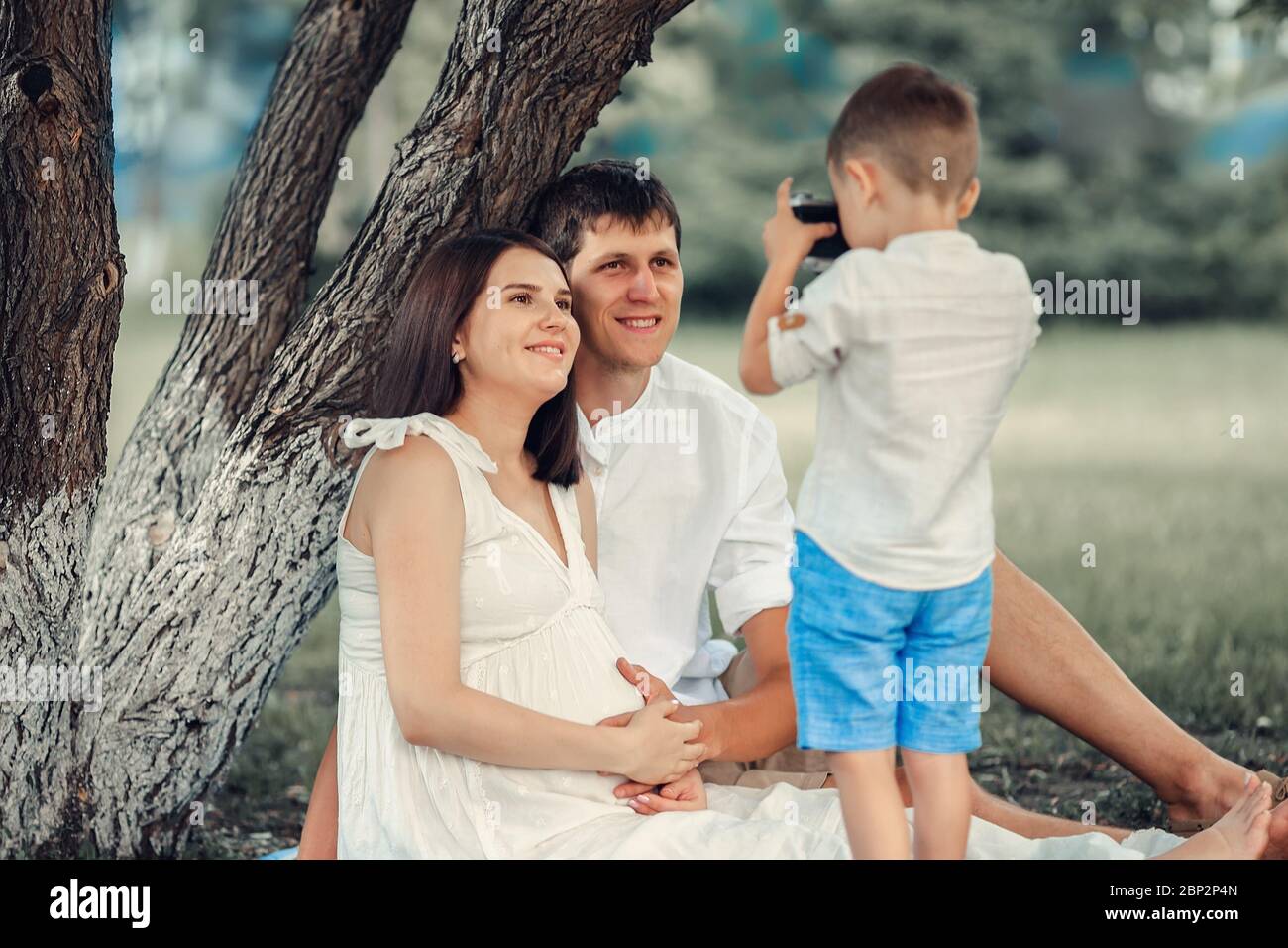 Ein junger Fotograf. Das Kind fotografiert an einem Sommertag unter einem Baum seine Mutter und seinen Vater. Stockfoto