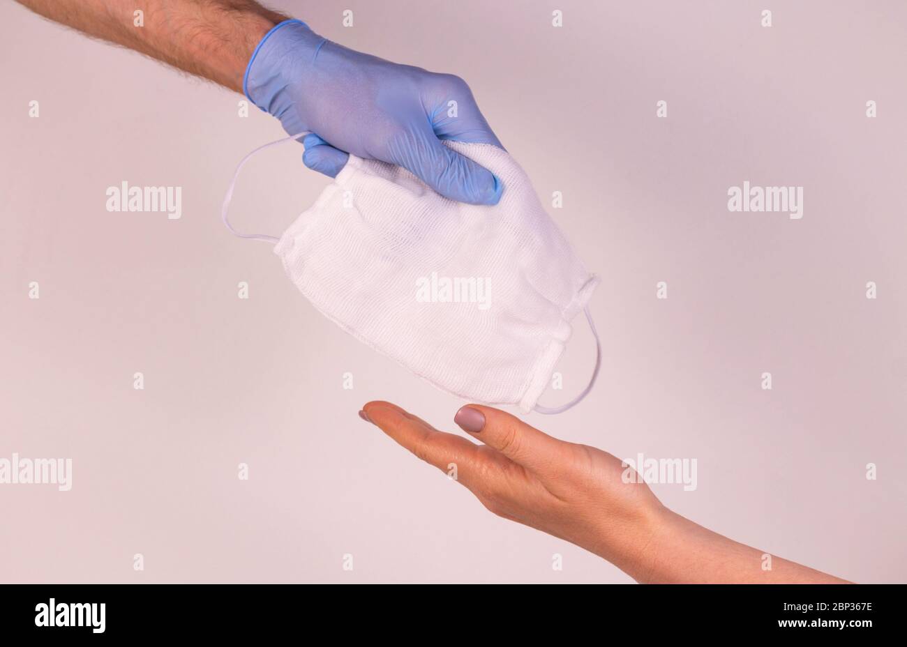 A hand in a blue glove gives a needy person a medical mask. Humanitarian aid. The concept of viral assistance Stockfoto