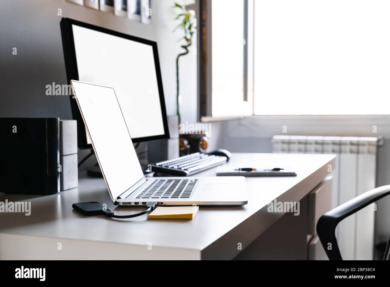 Arbeitsplatz für die Arbeit von zu Hause aus mit zwei Computern, einem Schreibtisch und einem offenen Fenster. Konzept für die Arbeit im Abstand. Stockfoto