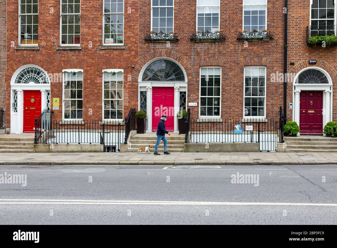 Dublin, Irland. Mai 2020. Mann mit Gesichtsmaske geht mit einem Hund entlang der verlassenen Upper Merrion Street. Covid-19. Berühmte rote Türen von Dublin. Stockfoto