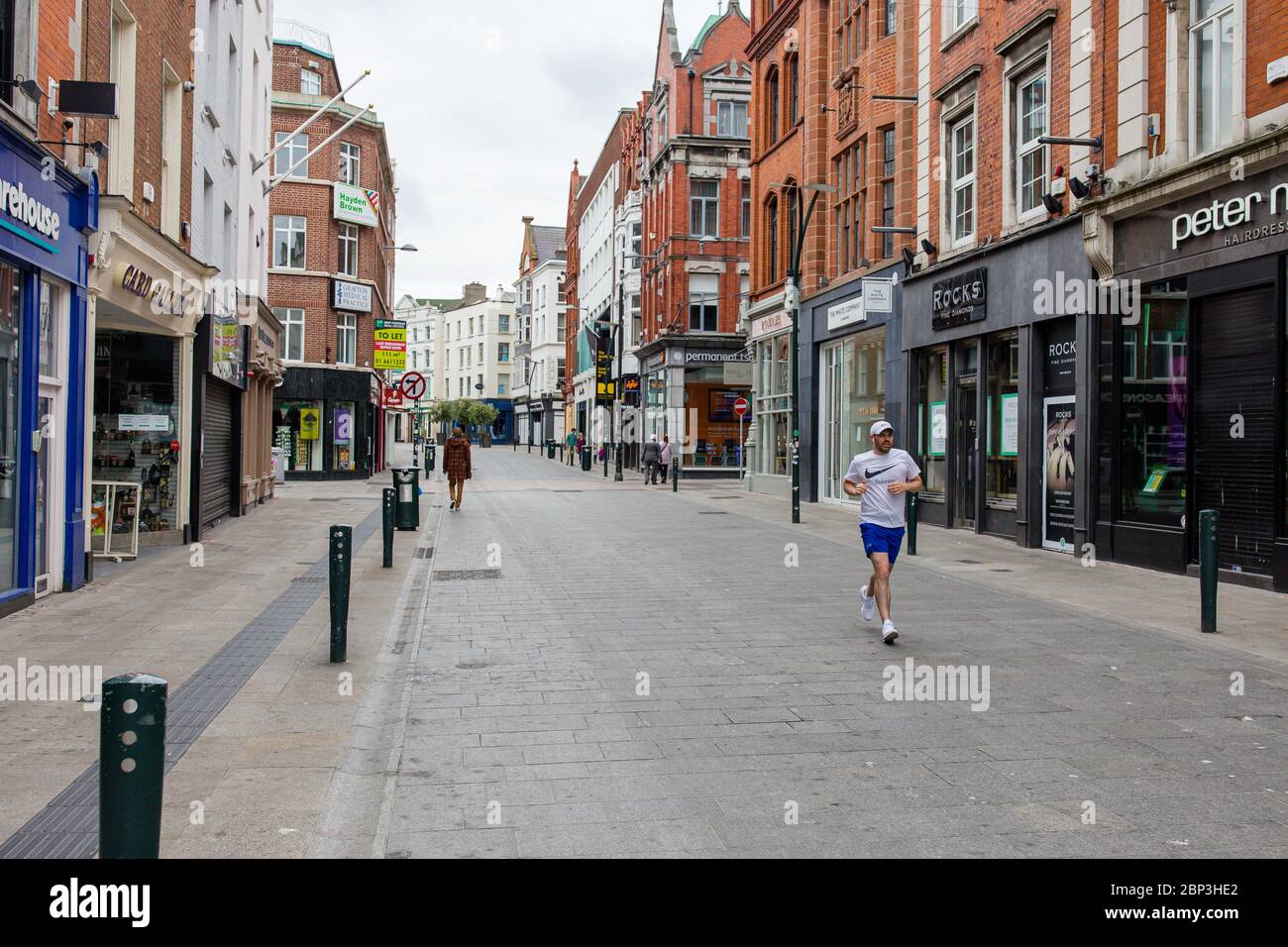 Fußgänger, die durch eine verlassene Grafton Street im Stadtzentrum von Dublin schlendern, da die Geschäfte wegen der Pandemie des Coronavirus geschlossen bleiben. Stockfoto