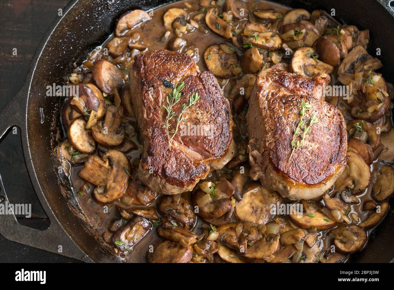 Filet Mignon in Pilzweinsauce: Zwei Filet Mignon Steaks mit einer cremigen Pilzsauce in einer gusseisernen Pfanne garniert mit frischen Thymian-Zweige Stockfoto