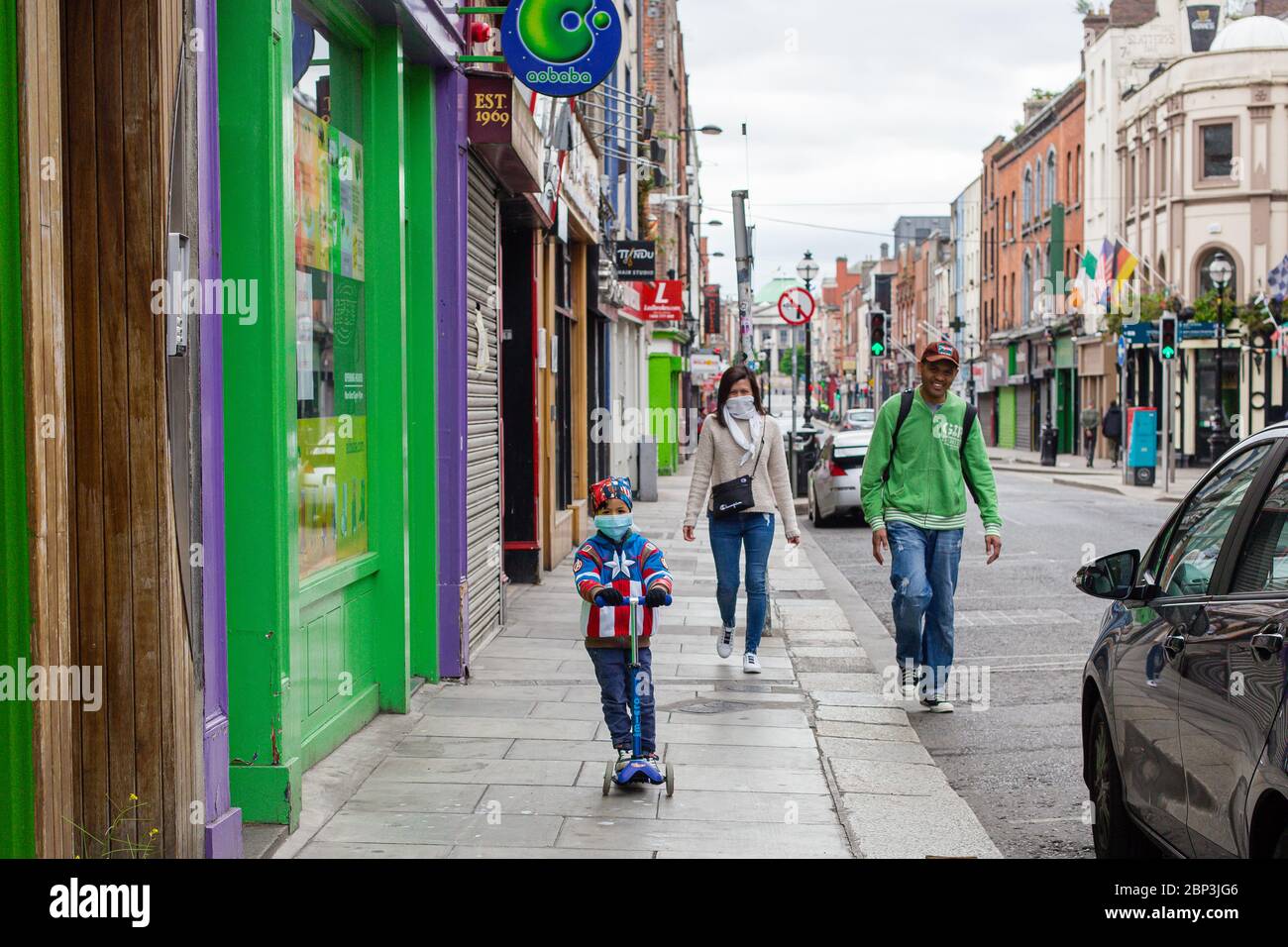 Junge auf einem Roller mit einer Superheldenjacke und einer schützenden Gesichtsmaske, die während der COVID-19-Pandemie mit seinen Eltern im Stadtzentrum von Dublin Sightseeing ist Stockfoto