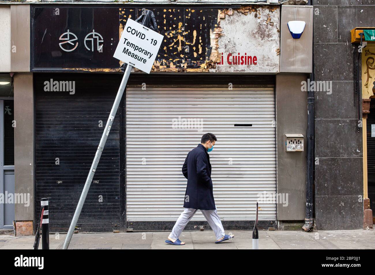 Asian Mann trägt Schutzmaske vorbei geschlossen Shop und schiefen Zeichen - Covid-19 vorübergehende Maßnahme. Wirtschaftliche Auswirkungen des Coronavirus Irland. Stockfoto