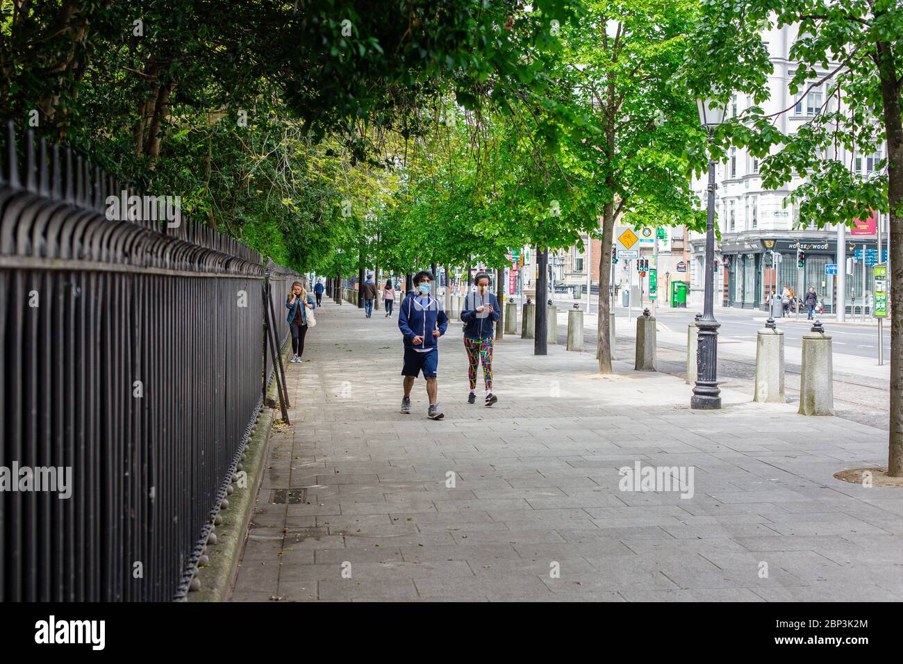 Fußgänger, die in Dublin mit Gesichtsmasken spazieren und die soziale Distanzierungsregel einhalten, indem sie im Freien in öffentlichen Bereichen Sicherheitsabstand einhalten. Stockfoto