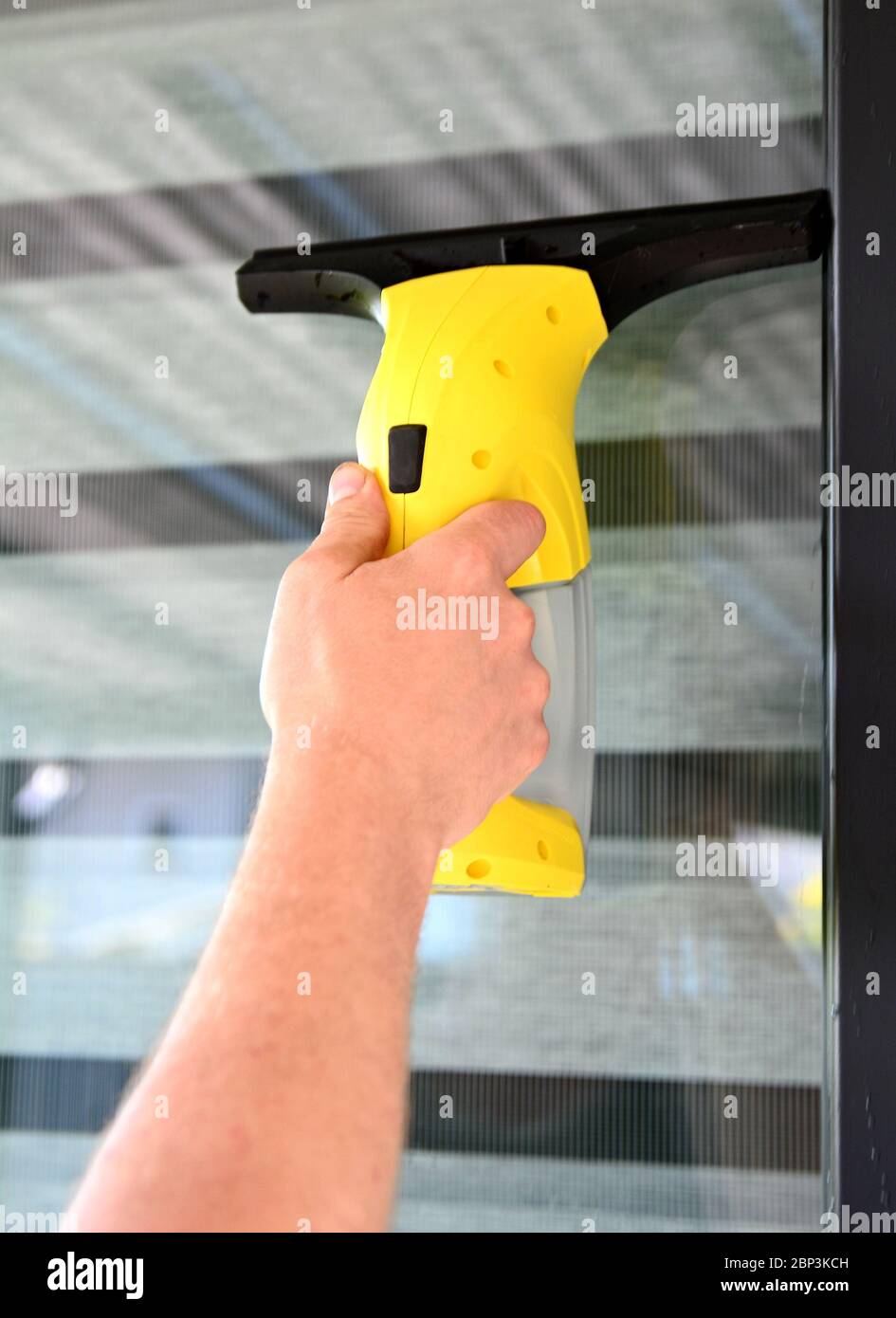 Reinigungsfenster mit kabellosem Elektrostaubsauger. Mann hält und benutzt Staubsauger. Stockfoto