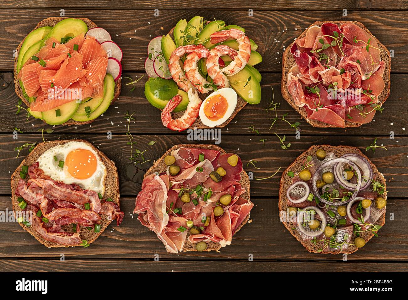 Sechs traditionelle dänische Smorrebrods, die mit verschiedenen Mahlzeiten serviert werden, sind in Holzuntergrund Stockfoto