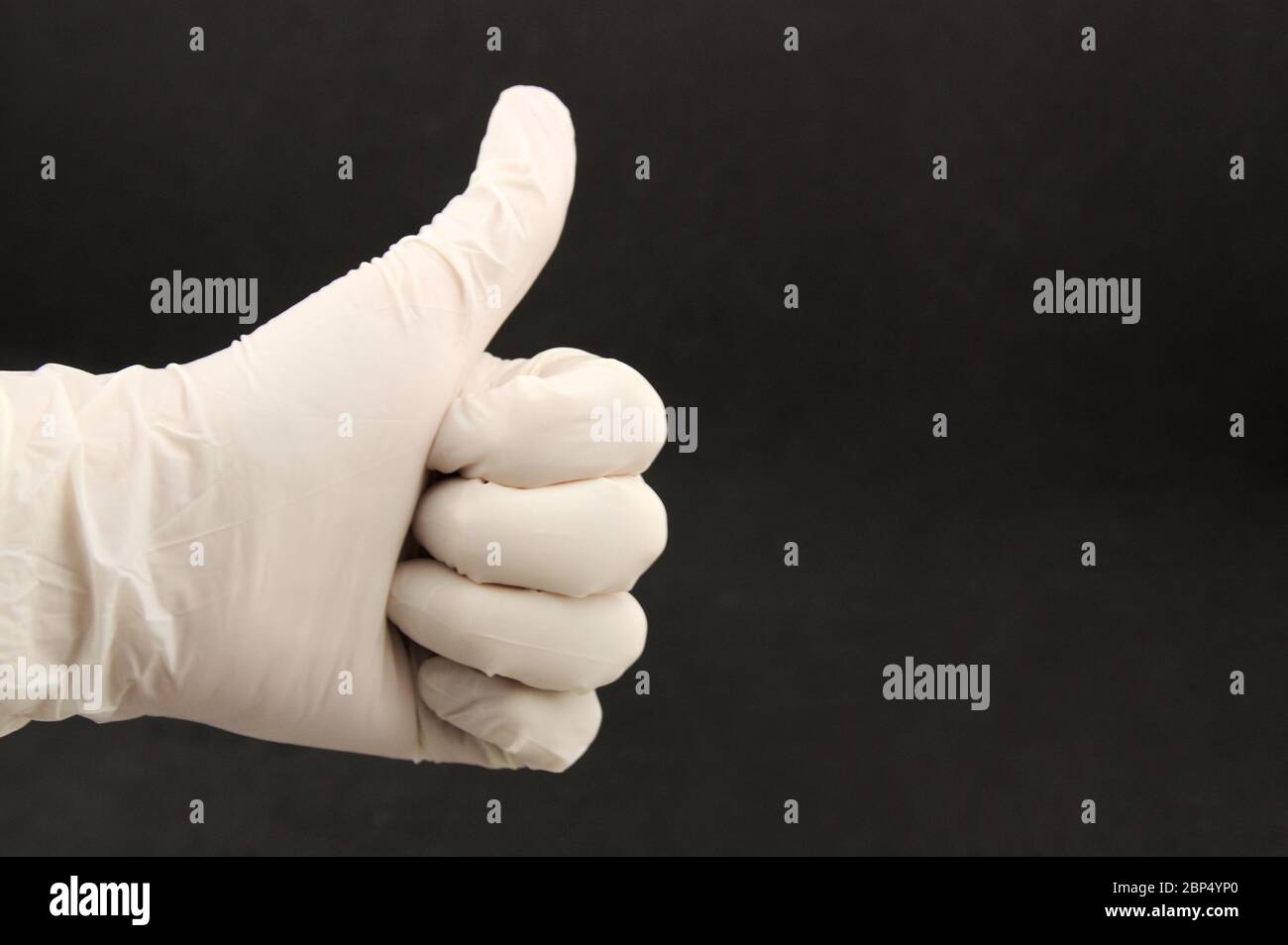 Eine Faust mit einem Latexhandschuh mit Daumen nach oben, schwarzem Hintergrund und Platz für Texte (Text kopieren) Stockfoto