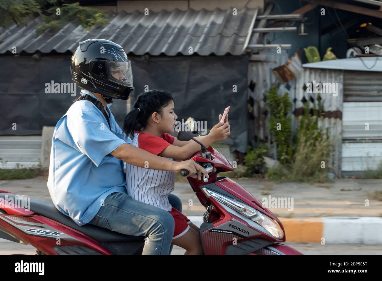 SAMUT PRAKAN, THAILAND, APR 04 2020, EIN Mann fährt mit einem Motorrad, während Mädchen auf ihr Handy gucken. Papa mit Tochter auf Motorroller Fahrten auf der Straße der Stadt. Stockfoto