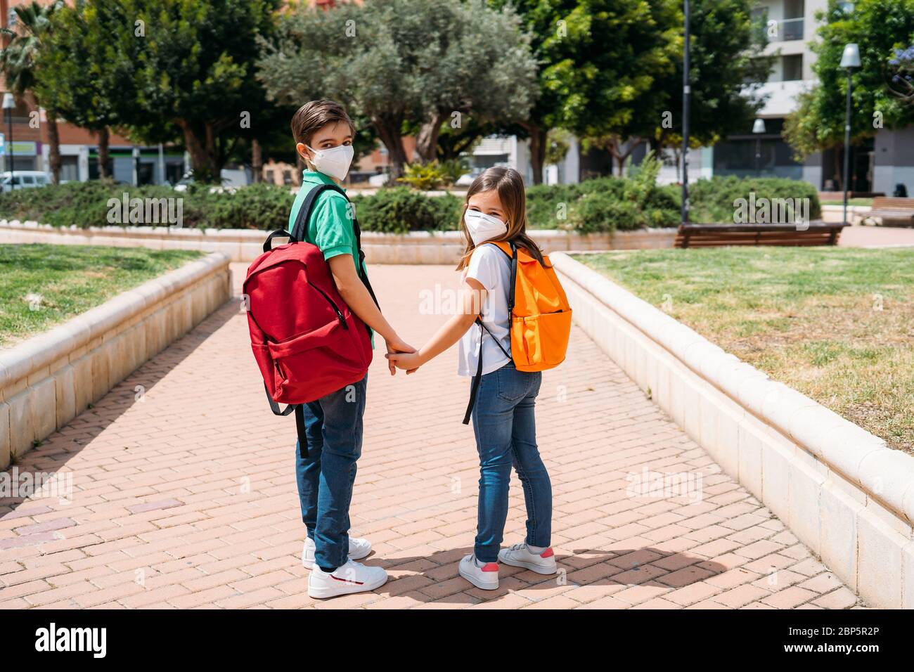 Junge und Mädchen mit Rucksäcken und Masken gehen zur Schule in Coronavirus Pandemie Stockfoto