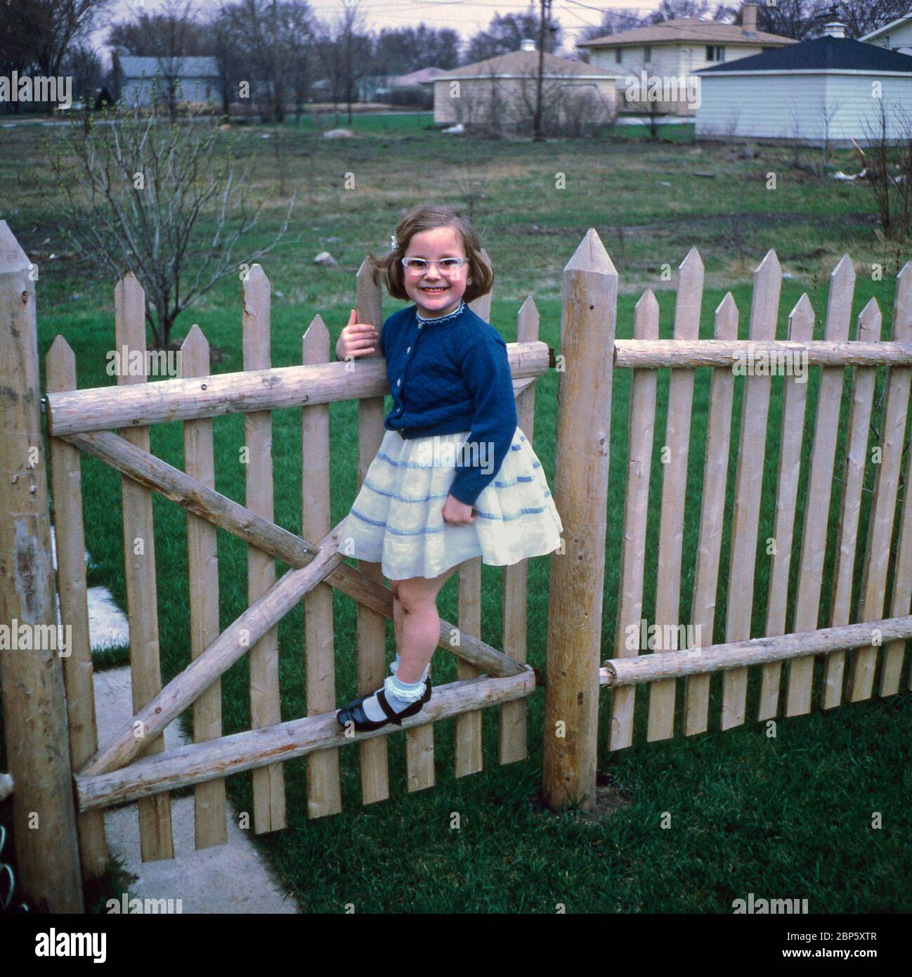 Ein glückliches junges Mädchen in ihrem Partykleid schwingt aus einem Tor in ihrem Garten, USA 1967. Stockfoto