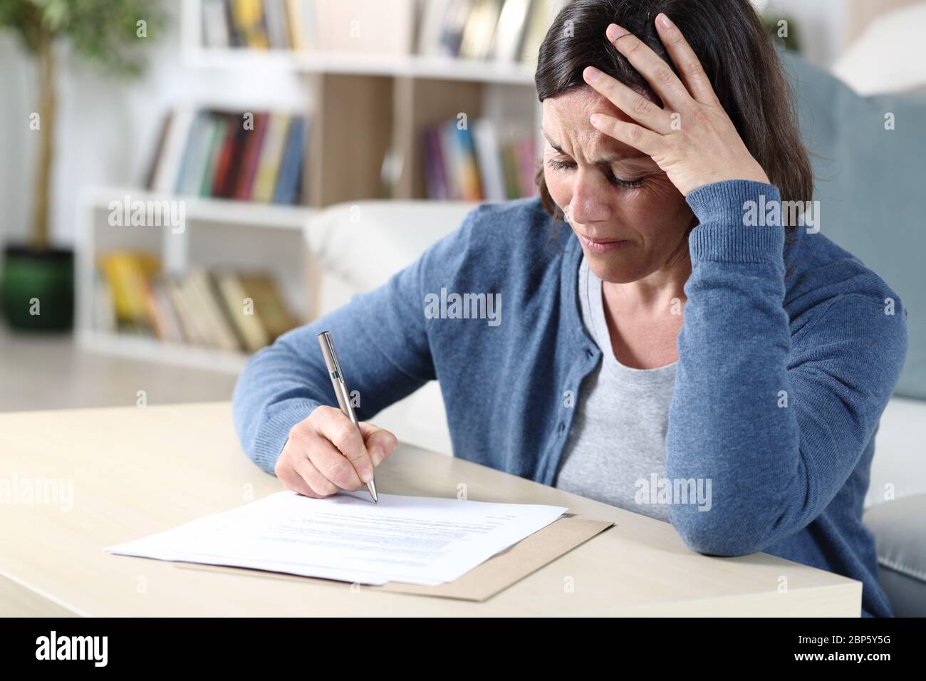 Traurige Frau mittleren Alters Signing Dokument beschwert sitzen im Wohnzimmer zu Hause Stockfoto