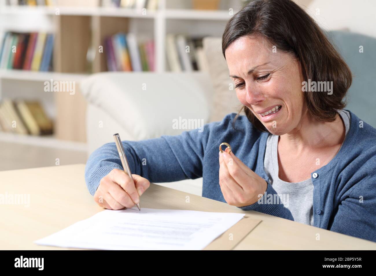 Traurige Frau weinend Unterzeichnung Scheidung Papiere Blick auf Ehering im Wohnzimmer zu Hause Stockfoto
