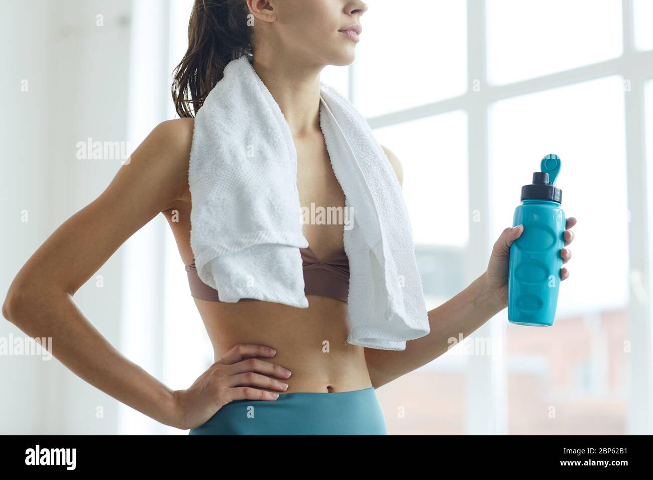 Cropped Portrait der fit junge Frau hält Wasserflasche während am Fenster nach dem Sport-Training stehen Stockfoto