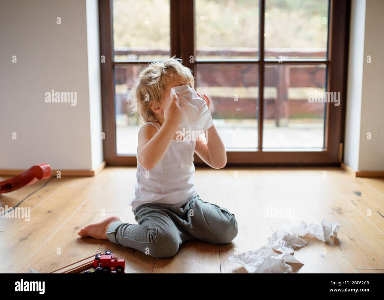 Kleiner kranker Junge mit Kälte zu Hause auf dem Boden sitzend, niest. Stockfoto