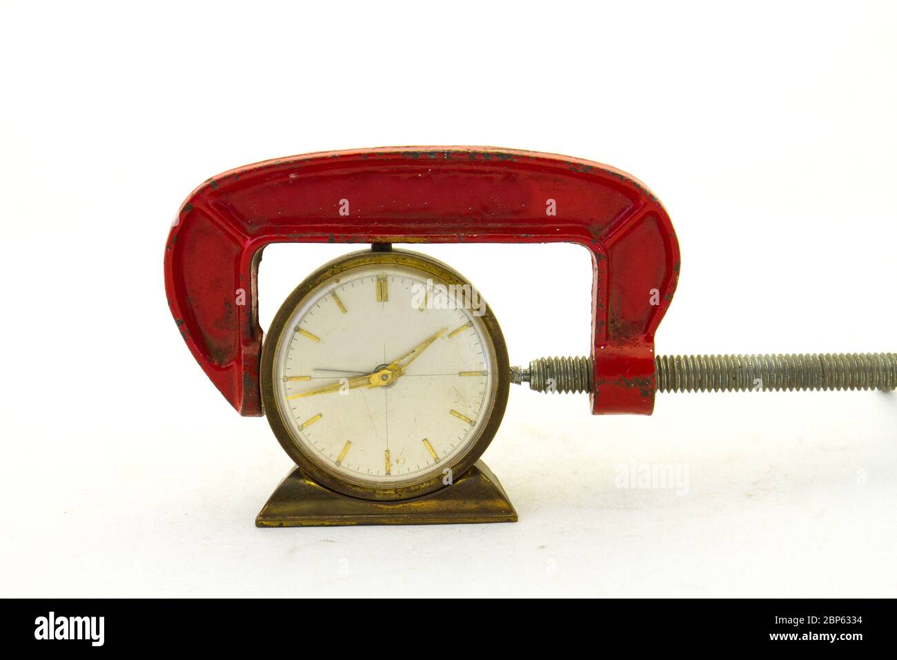 Eine alte Uhr im engen Griff einer roten Metallklemme isoliert auf einem klaren Hintergrundbild mit Kopierraum Stockfoto