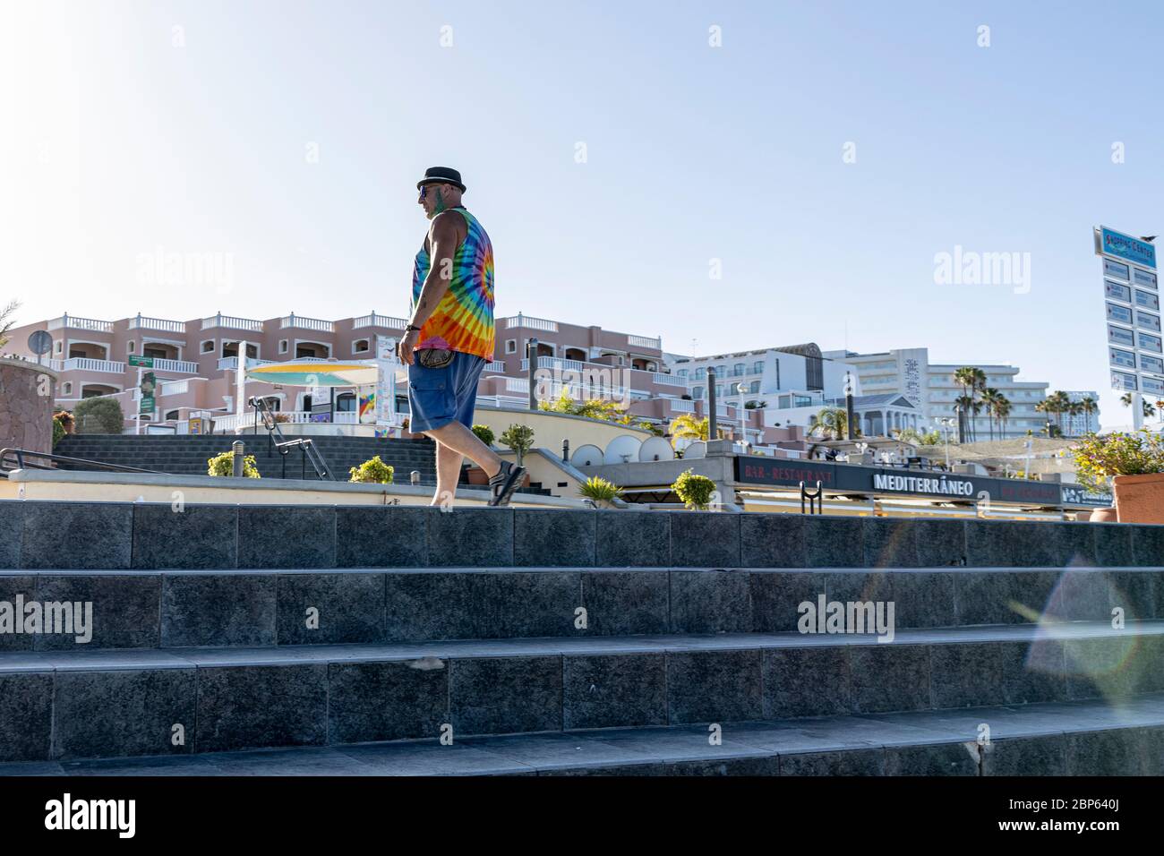 Mann mit Schweinebätenhut, gefärbtem grünen Bart und T-Shirt mit Tie-Dye-Farbe geht während der ersten Phase der Deeskalation des Covid 19 auf der Promenade am Playa Fanabe spazieren Stockfoto