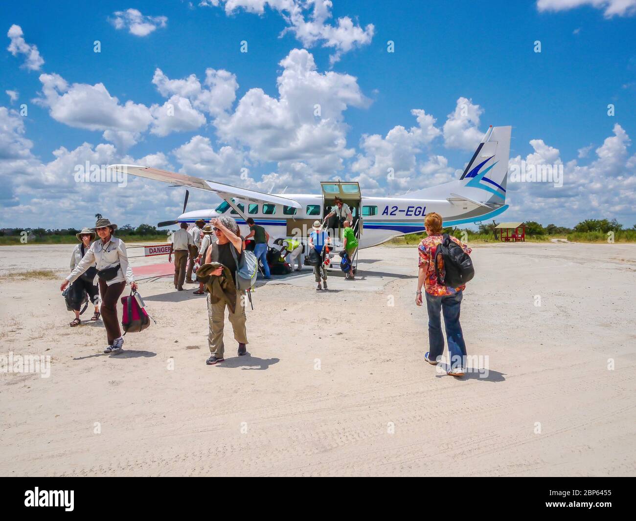 Okavango Delta, Botswana - 5. März 2013. Eine kleine Gruppe amerikanischer Safarigäste steigen an Bord eines leichten Flugzeugs auf einer ländlichen Landepiste in Afrika aus. Stockfoto