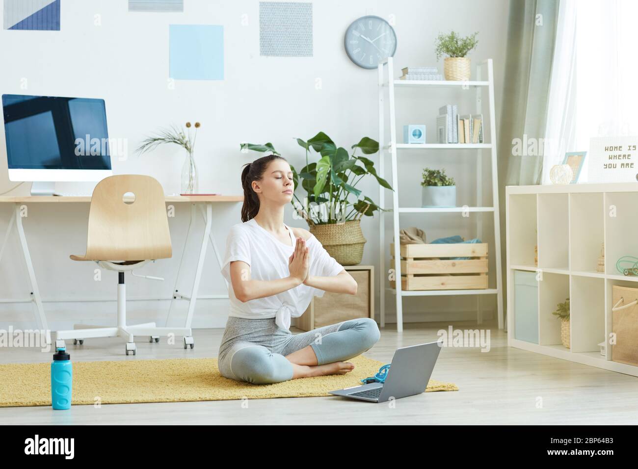 Ganzkörperportrait der zeitgenössischen jungen Frau beim Yoga, während sie in Lotusstellung zu Hause sitzt, kopieren Raum Stockfoto