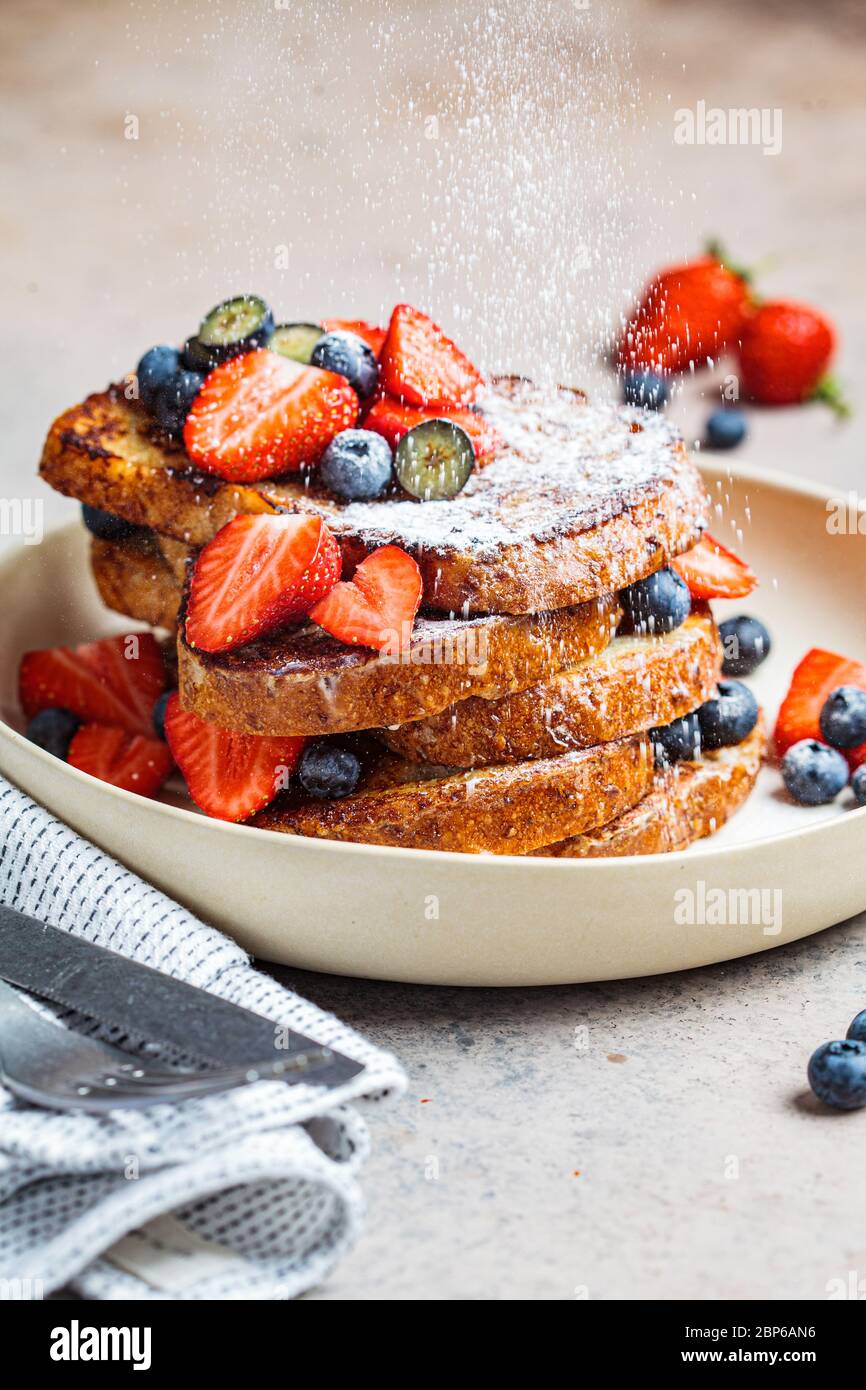 Traditioneller französischer Toast mit Heidelbeeren, Erdbeeren und Puderzucker auf einem weißen Teller. Stockfoto