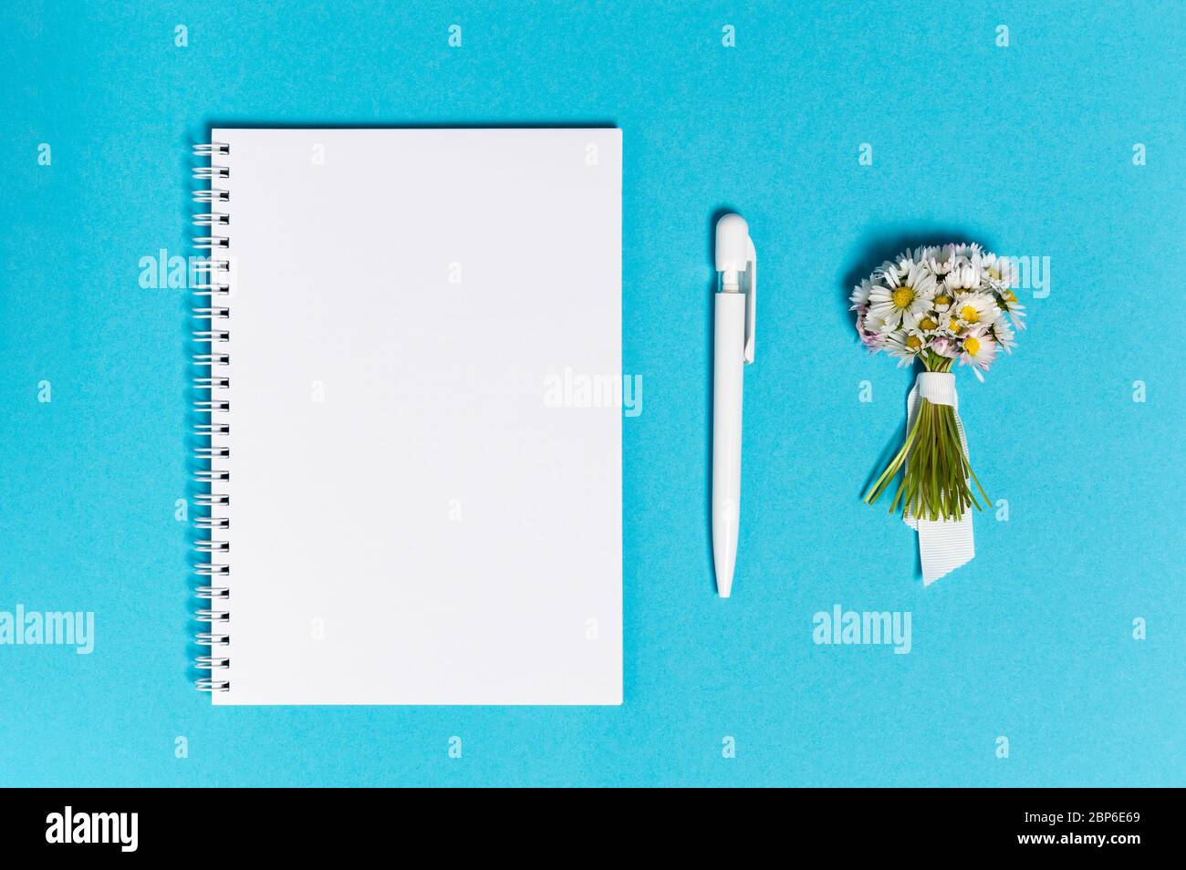 Notizbuch mit leerem Papier, Stift und Blumenstrauß auf blauem Hintergrund von oben. Freiberufliche, schriftliche oder Urlaubsplanung Konzept. Flach mit Stockfoto