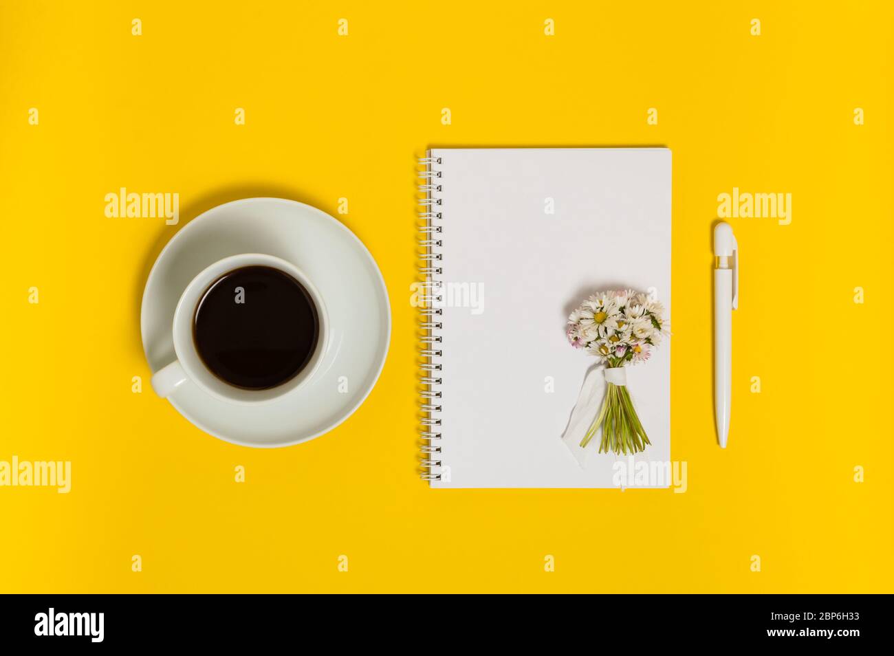 Tasse schwarzen Kaffee, Notizbuch mit leerem Papier, Stift und Strauß Gänseblümchen auf gelbem Hintergrund von oben. Schreiben oder Urlaub Planung Konzept. F Stockfoto