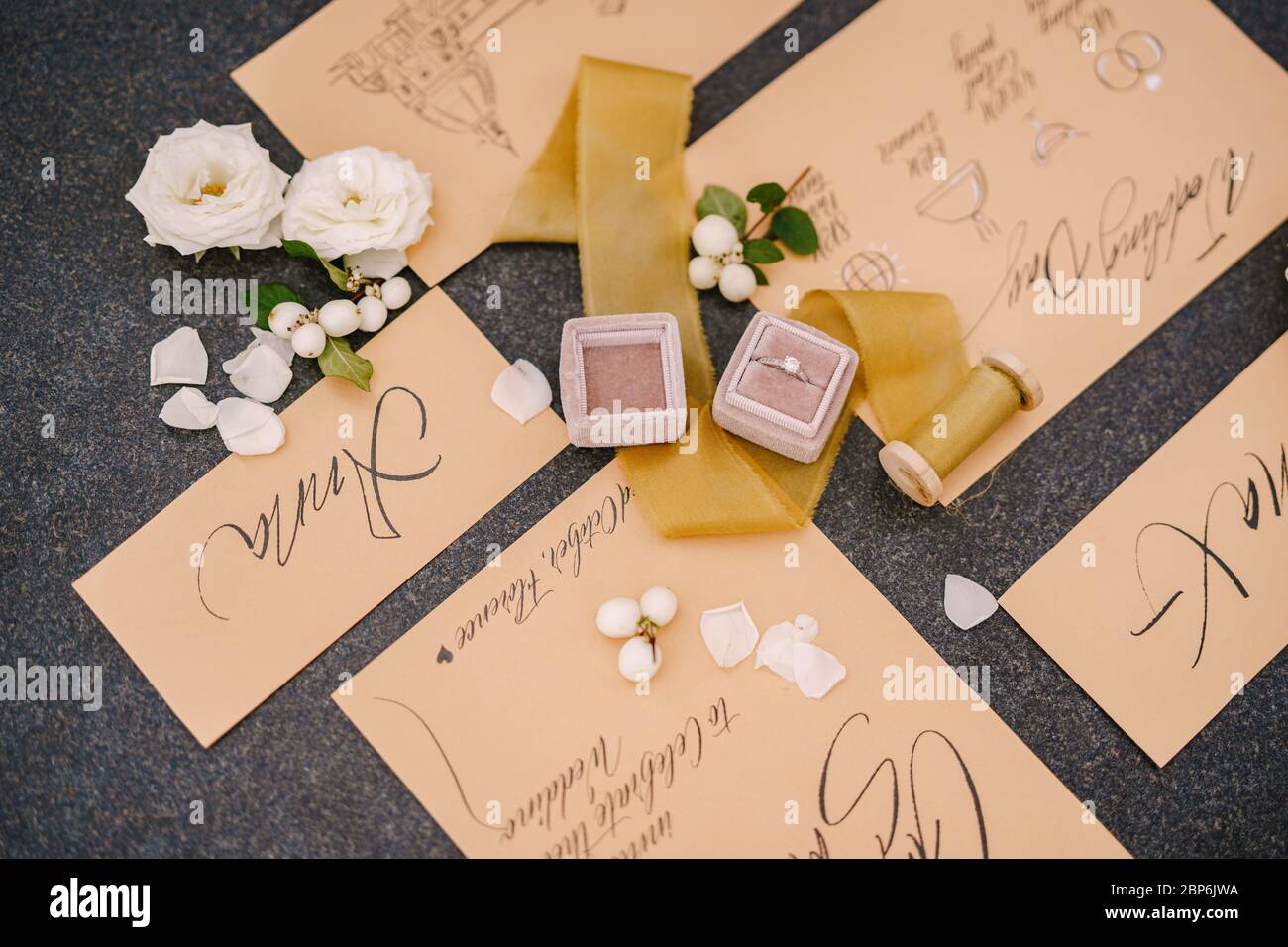 Eheringe in einer Schachtel, Einladungskarten, Seidenband, weiße Rosen auf schwarzem Hintergrund. Ansicht von oben. Stockfoto