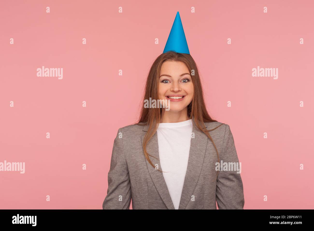 Porträt von glücklichen freudigen Frau im Business-Anzug und mit Party-Kegel auf dem Kopf lächelnd in der Kamera, Geburtstagsfeier, Job-Promotion. In Stockfoto
