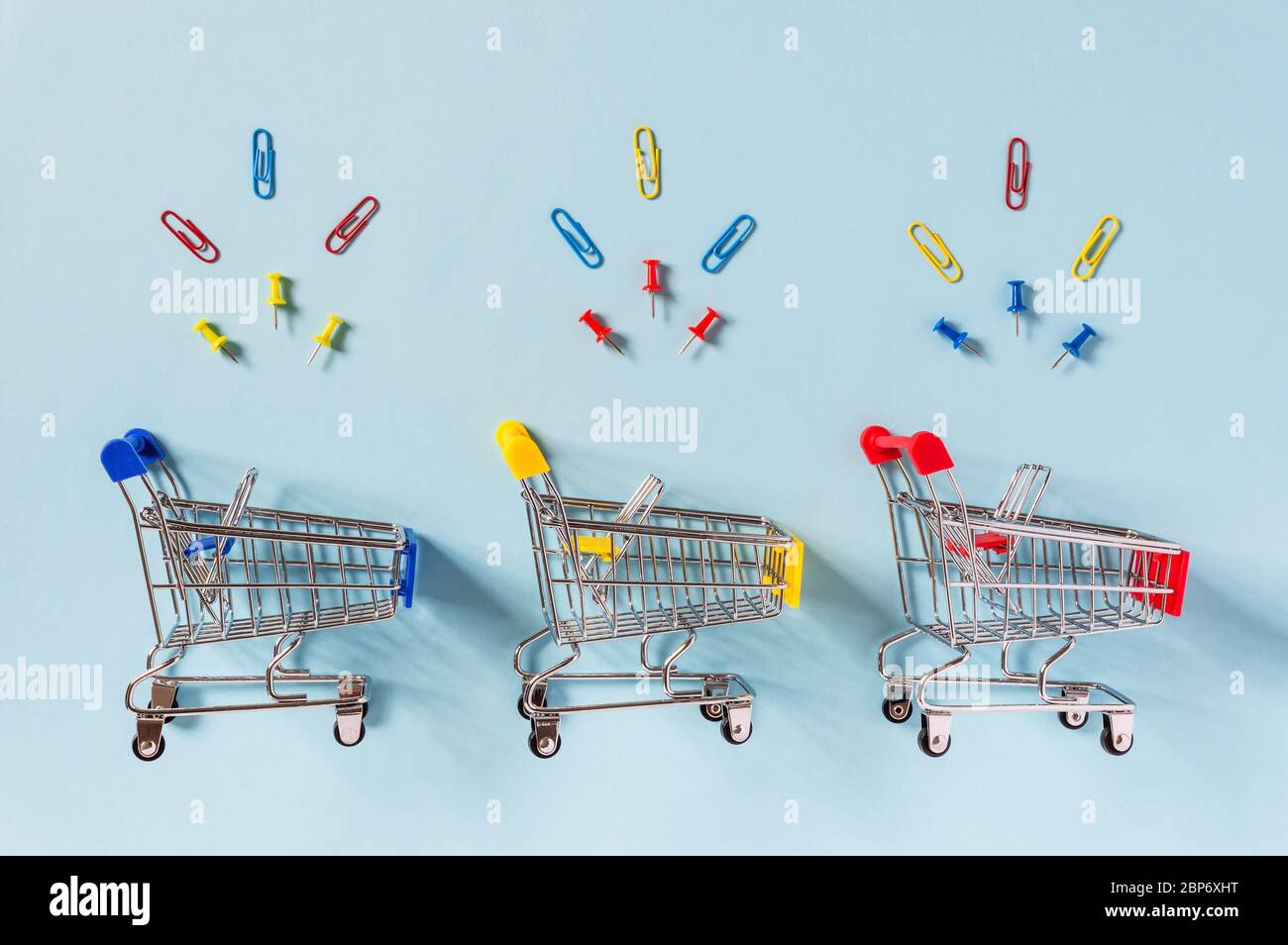 Bunte Supermarkt-Einkaufswagen auf blauem Hintergrund mit gelben, roten und blauen Clips und Pins oben. Einkaufen für Bürobedarf, Handel Stockfoto