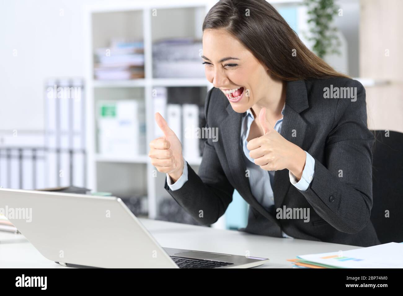 Glückliche Geschäftsführerin mit Daumen nach oben auf Videocall auf Laptop, die auf ihrem Schreibtisch im Büro sitzt Stockfoto