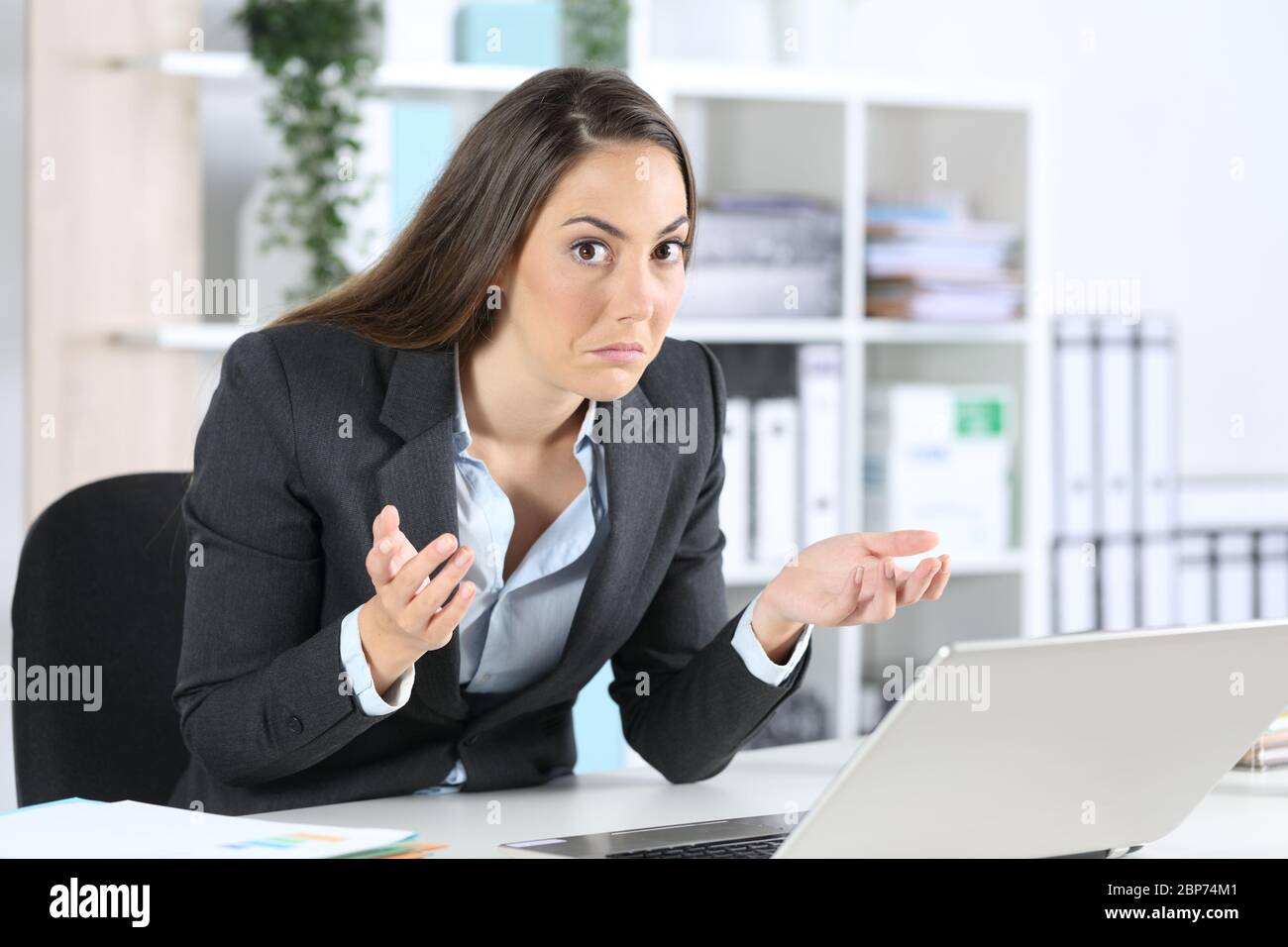 Verwirrt Geschäftsfrau Blick auf Kamera mit Laptop sitzt auf ihrem Schreibtisch im Büro Stockfoto