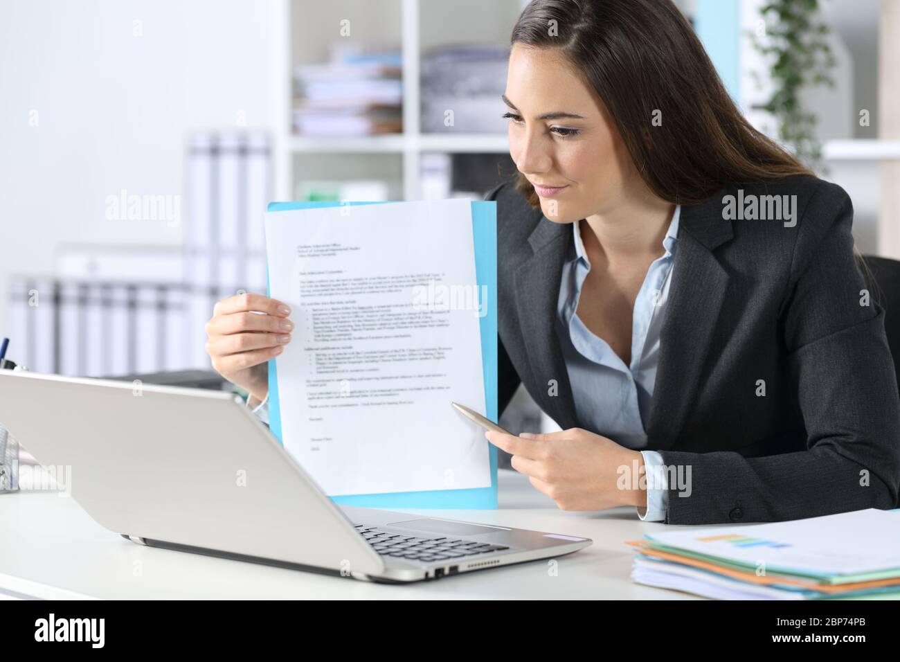 Executive Frau zeigt Vertrag auf Videocall auf Laptop sitzt auf ihrem Schreibtisch im Büro Stockfoto