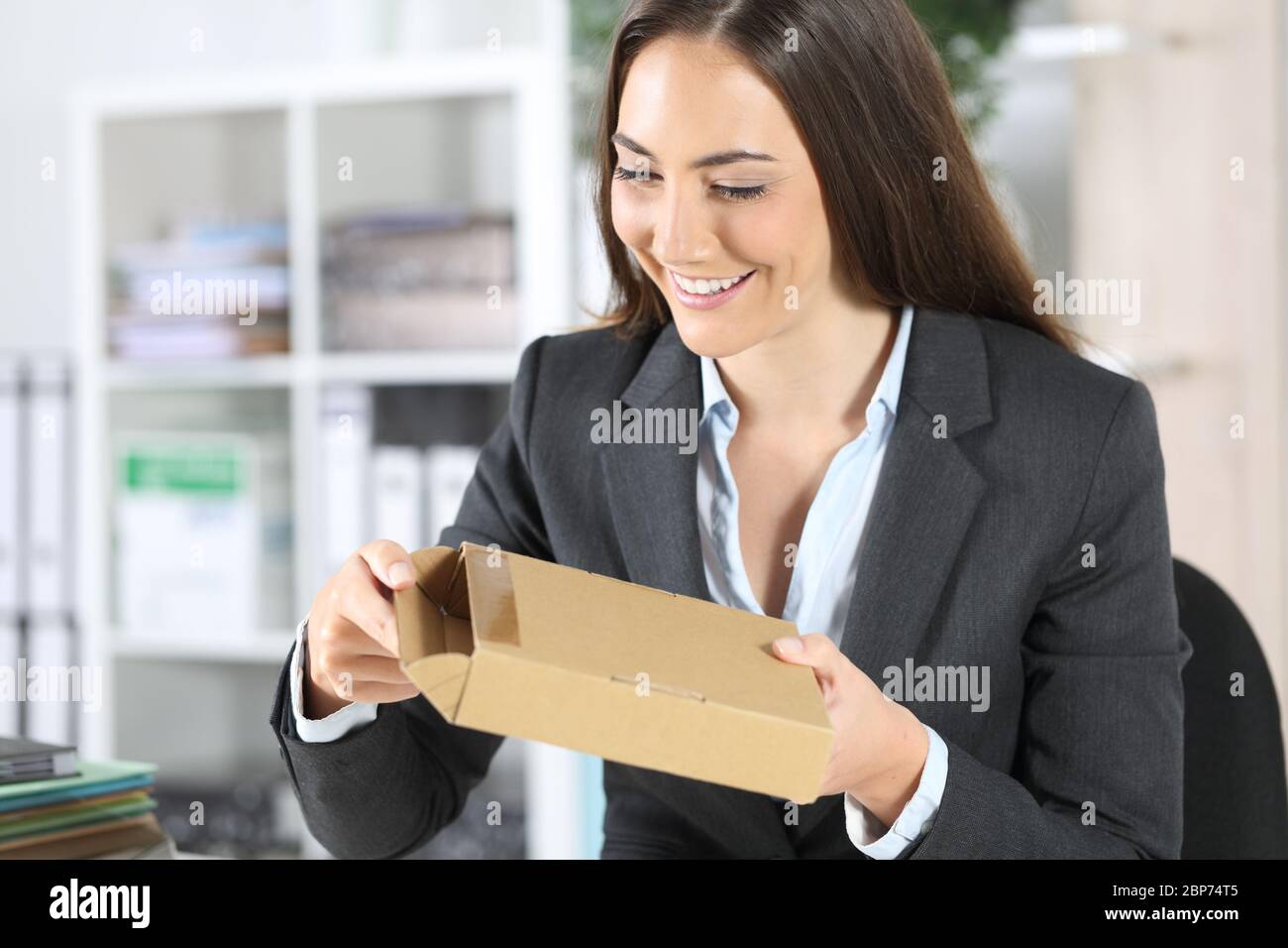 Glückliche Exekutive Frau Eröffnung Paket Lieferung sitzt auf einem Schreibtisch im Büro Stockfoto