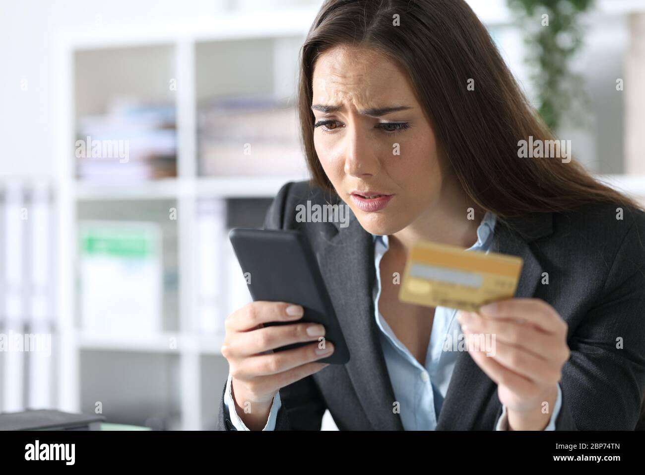 Besorgte Exekutive Frau, die mit Smartphone und Kreditkarte im Büro bezahlt Stockfoto